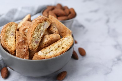 Photo of Tasty almond biscuits (Cantuccini) in bowl and nuts on light marble table, closeup. Space for text