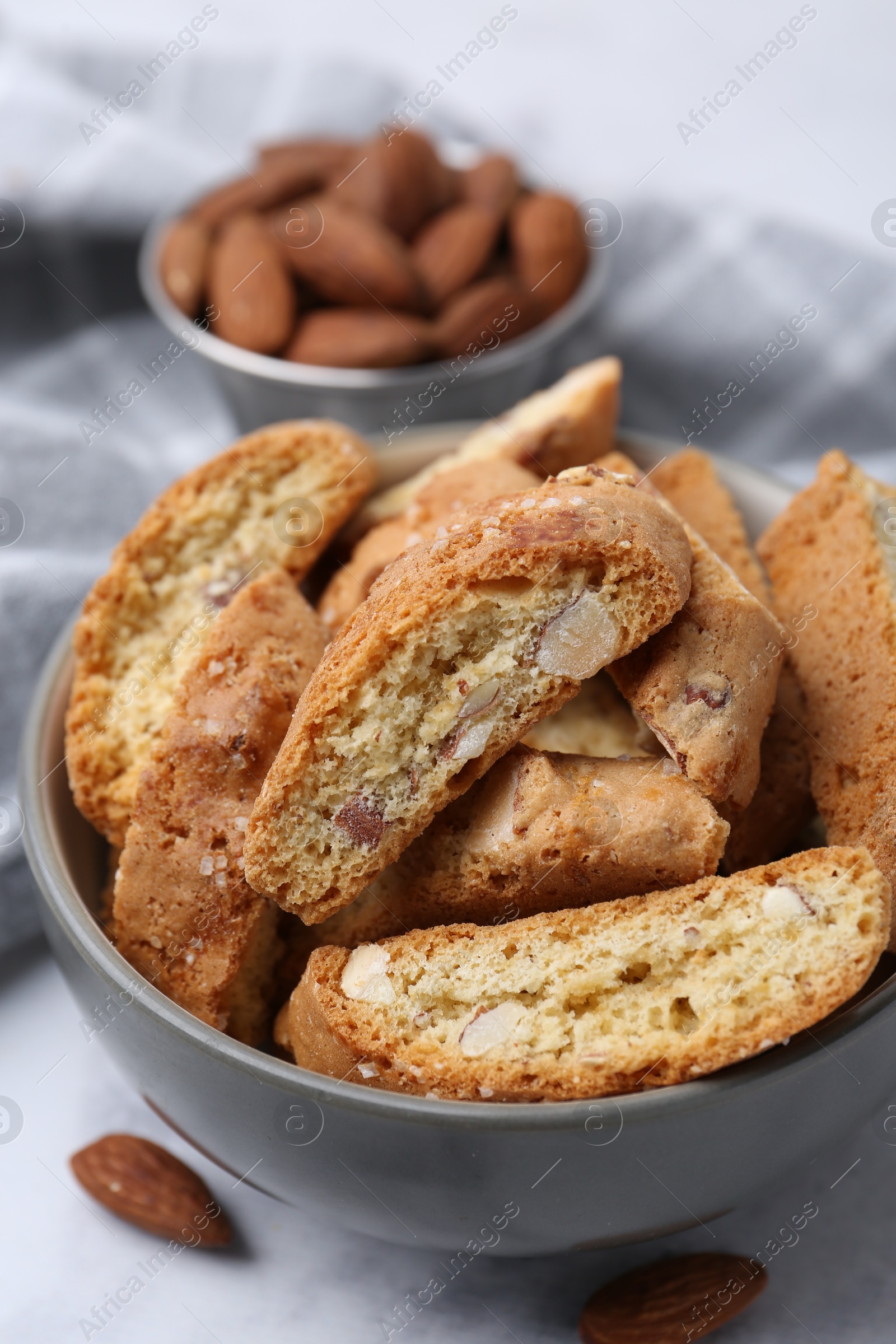 Photo of Tasty almond biscuits (Cantuccini) in bowl and nuts on light table, closeup