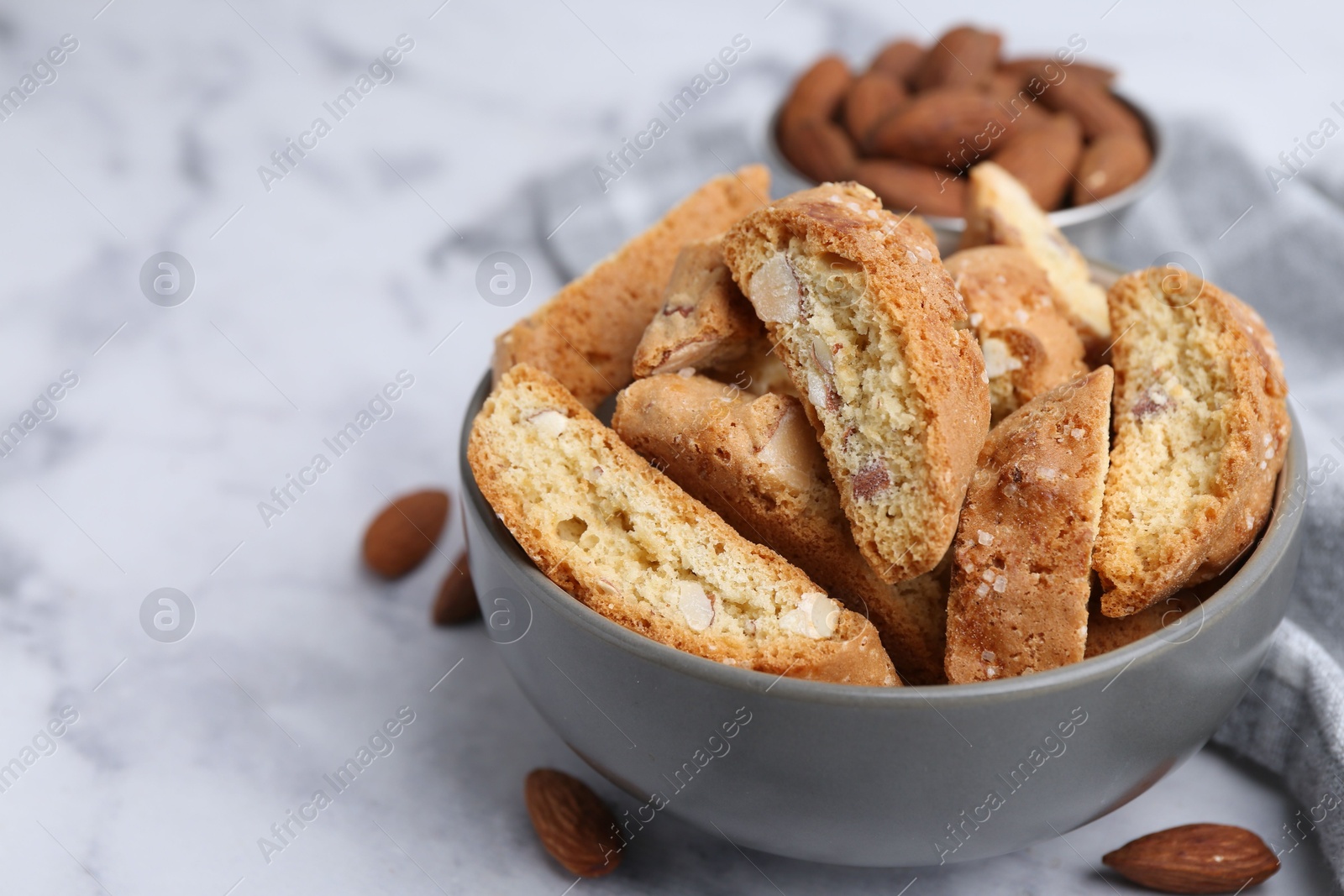 Photo of Tasty almond biscuits (Cantuccini) in bowl and nuts on light marble table, closeup. Space for text