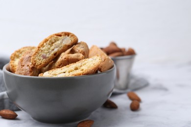 Photo of Tasty almond biscuits (Cantuccini) in bowl and nuts on light table, closeup. Space for text