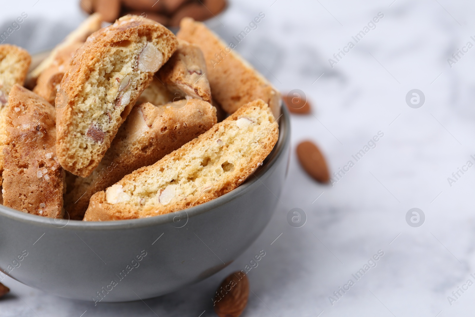 Photo of Tasty almond biscuits (Cantuccini) in bowl and nuts on light table, closeup. Space for text