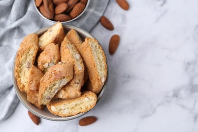 Photo of Tasty almond biscuits (Cantuccini) in bowl and nuts on light marble table, flat lay. Space for text