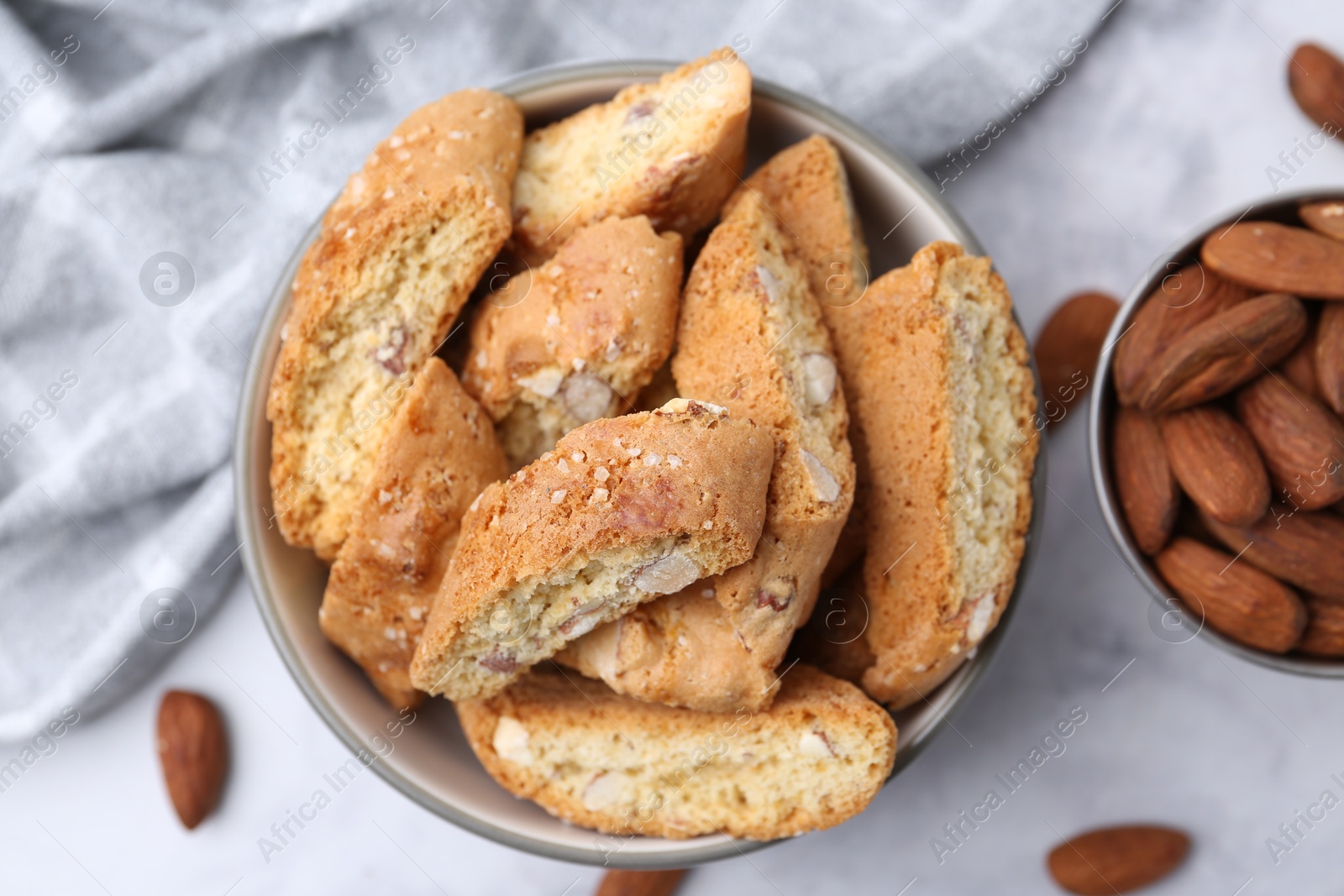 Photo of Tasty almond biscuits (Cantuccini) in bowl and nuts on light table, flat lay