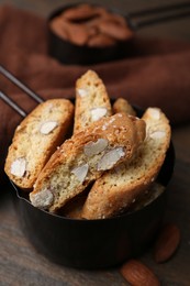 Photo of Tasty almond biscuits (Cantuccini) in scoop and nuts on wooden table, closeup