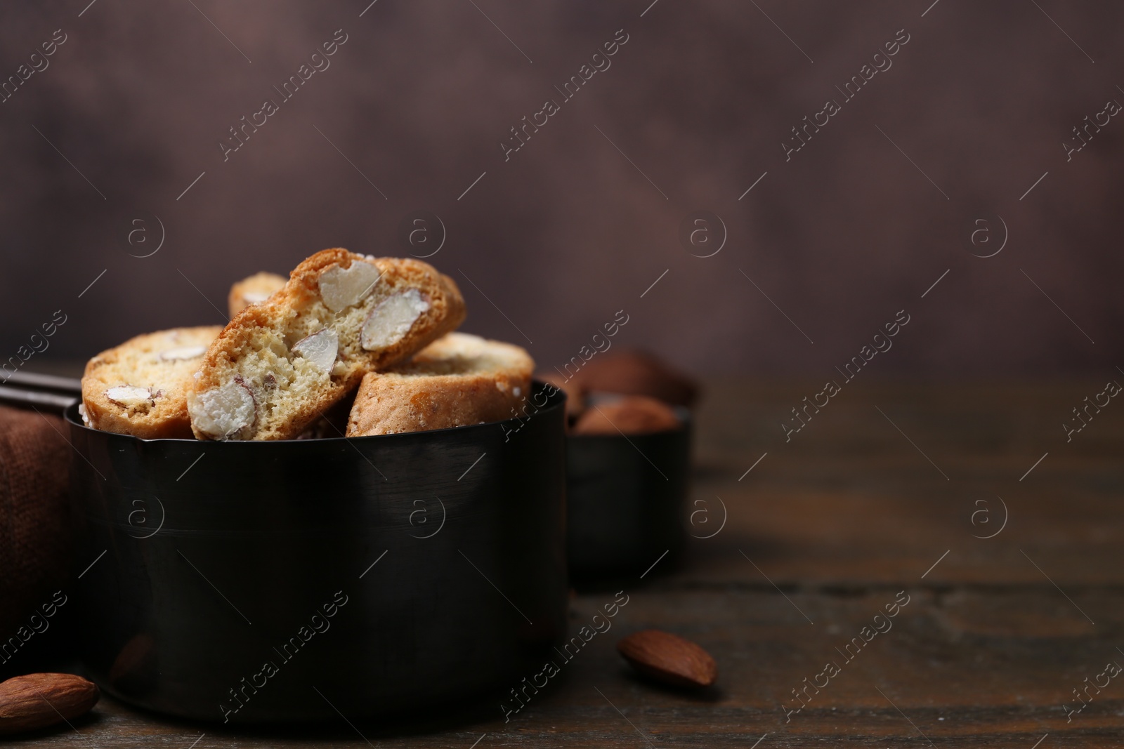 Photo of Tasty almond biscuits (Cantuccini) in scoop and nuts on wooden table, closeup. Space for text