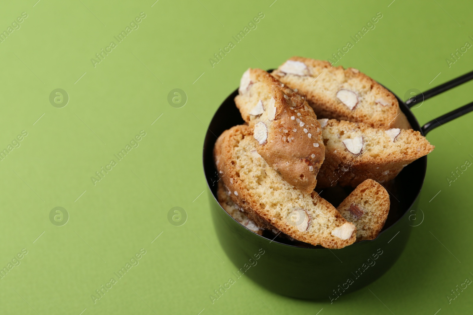 Photo of Tasty almond biscuits (Cantuccini) in scoop on green background, closeup. Space for text