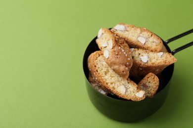 Photo of Tasty almond biscuits (Cantuccini) in scoop on green background, closeup. Space for text