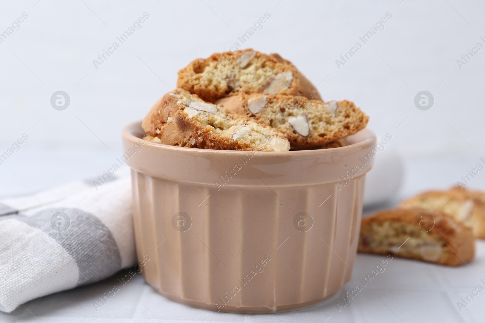 Photo of Tasty almond biscuits (Cantuccini) in bowl on white tiled table, closeup