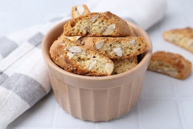 Photo of Tasty almond biscuits (Cantuccini) in bowl on white tiled table, closeup