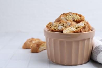 Photo of Tasty almond biscuits (Cantuccini) in bowl on white tiled table, closeup. Space for text