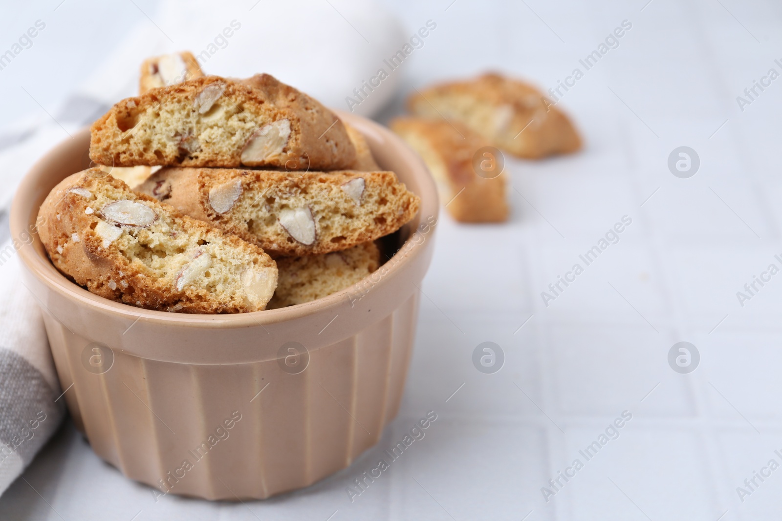 Photo of Tasty almond biscuits (Cantuccini) in bowl on white tiled table, closeup. Space for text