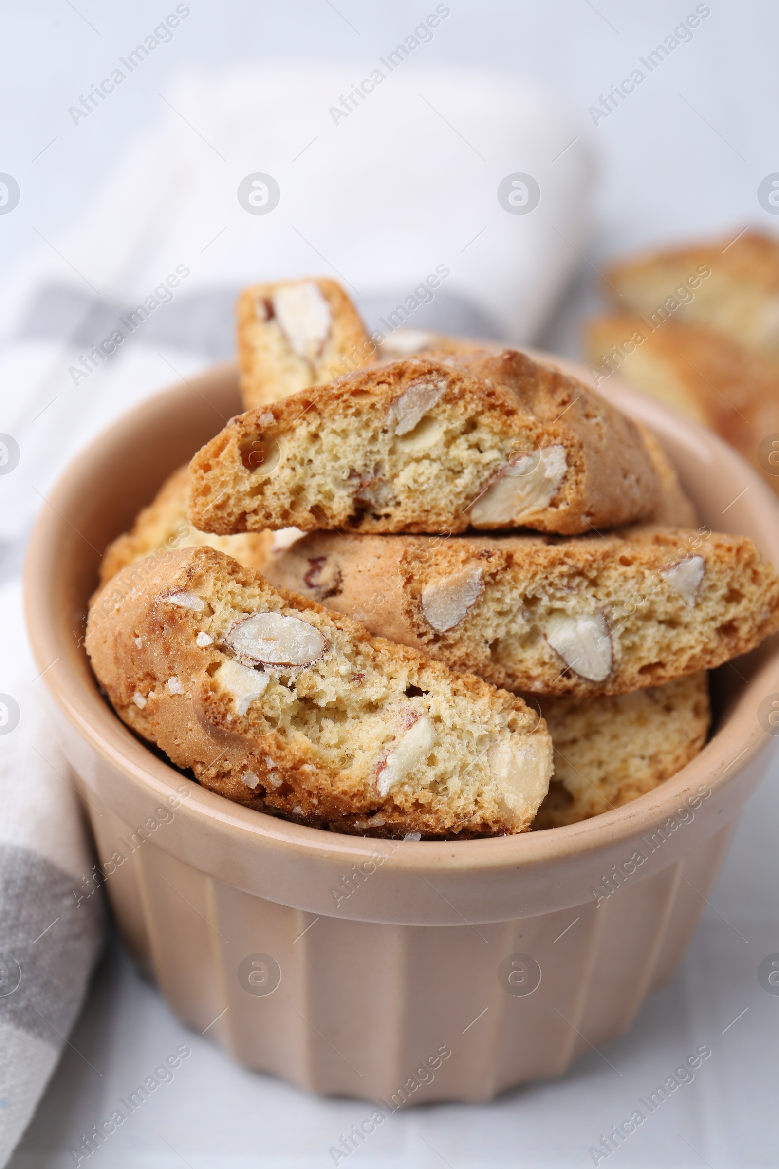 Photo of Tasty almond biscuits (Cantuccini) in bowl on white tiled table, closeup