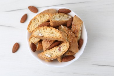 Photo of Tasty almond biscuits (Cantuccini) and nuts in bowl on white wooden table, top view