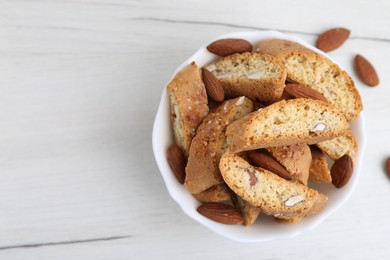 Photo of Tasty almond biscuits (Cantuccini) and nuts in bowl on white wooden table, top view. Space for text