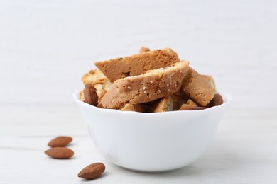 Photo of Tasty almond biscuits (Cantuccini) and nuts in bowl on white table, closeup