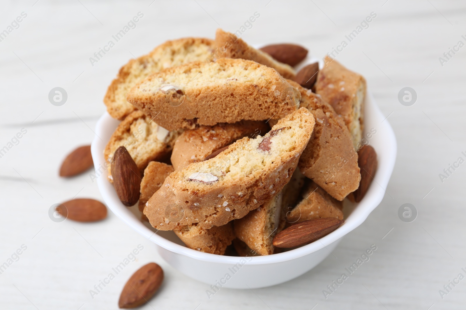 Photo of Tasty almond biscuits (Cantuccini) and nuts in bowl on white table, closeup