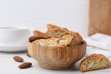 Photo of Tasty almond biscuits (Cantuccini) and nuts in bowl on white wooden table, closeup