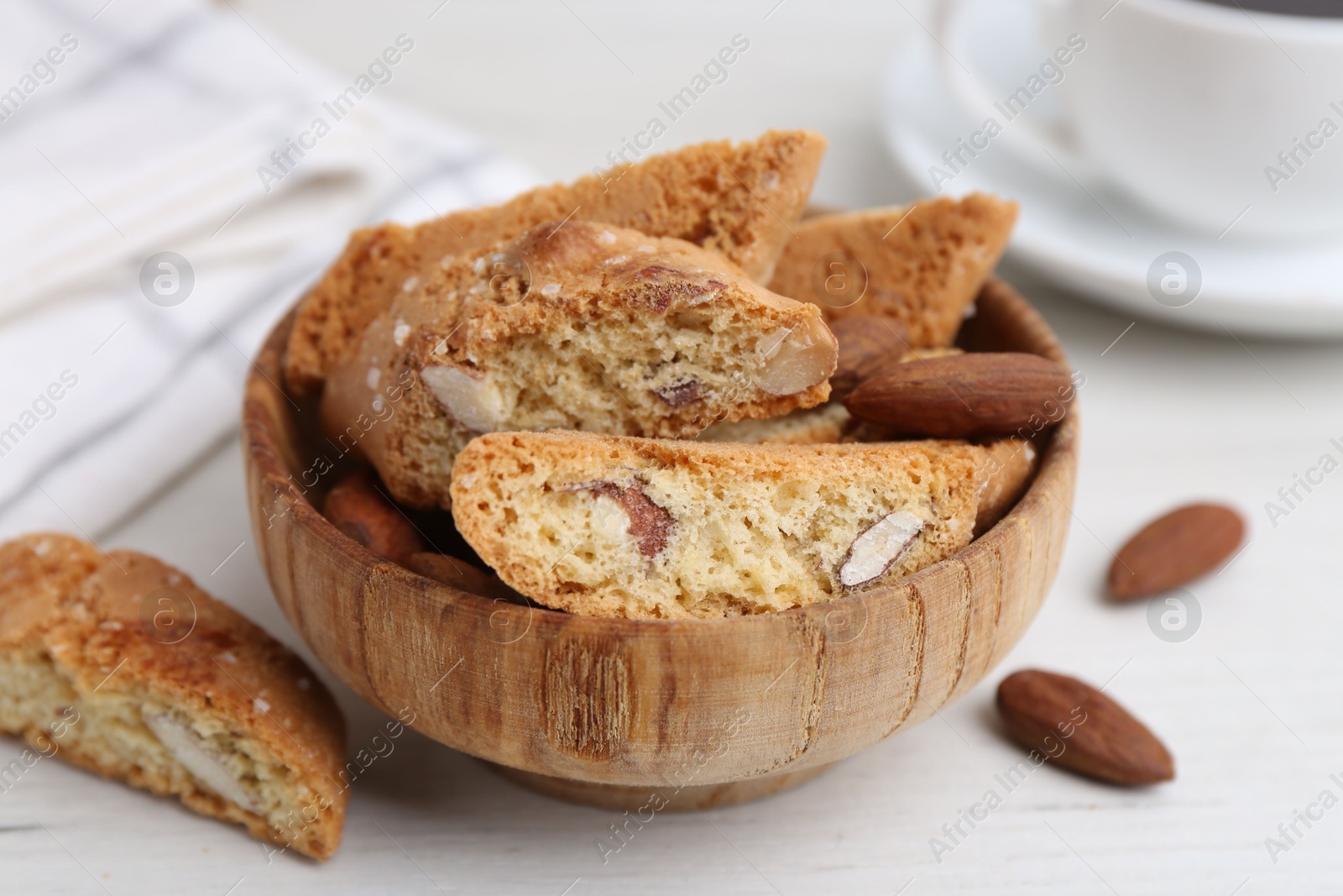 Photo of Tasty almond biscuits (Cantuccini) and nuts in bowl on white wooden table, closeup