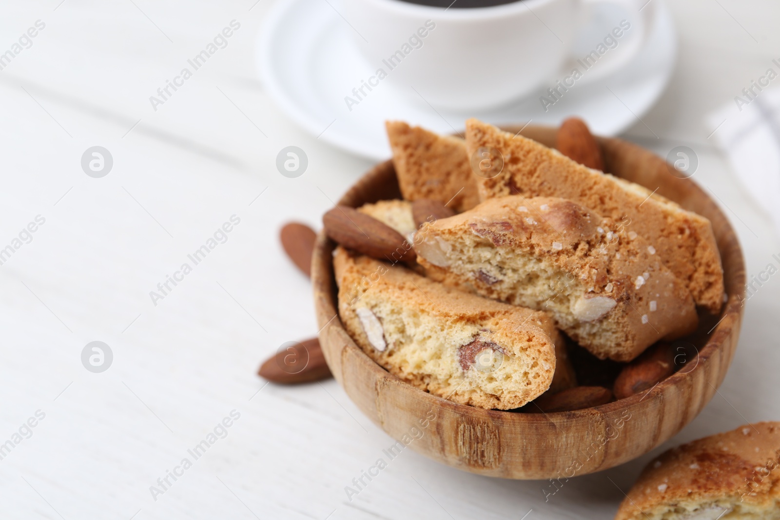 Photo of Tasty almond biscuits (Cantuccini) and nuts in bowl on white wooden table, closeup. Space for text