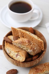 Photo of Tasty almond biscuits (Cantuccini), nuts and cup of coffee on white wooden table, closeup