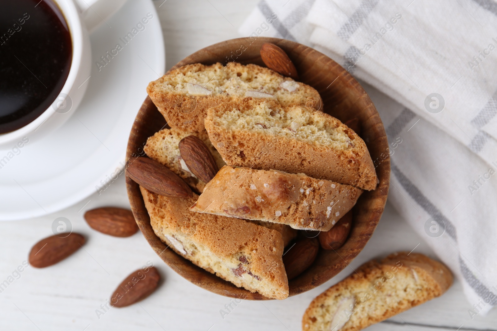 Photo of Tasty almond biscuits (Cantuccini), nuts and cup of coffee on white wooden table, flat lay