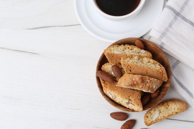 Photo of Tasty almond biscuits (Cantuccini), nuts and cup of coffee on white wooden table, flat lay. Space for text