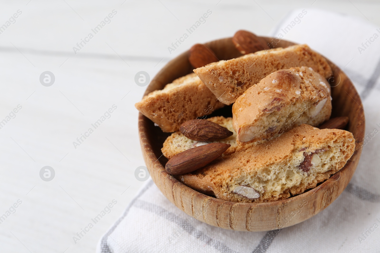 Photo of Tasty almond biscuits (Cantuccini) in bowl and nuts on white table, closeup. Space for text