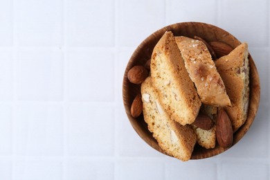 Photo of Tasty almond biscuits (Cantuccini) and nuts in bowl on white tiled table, top view. Space for text