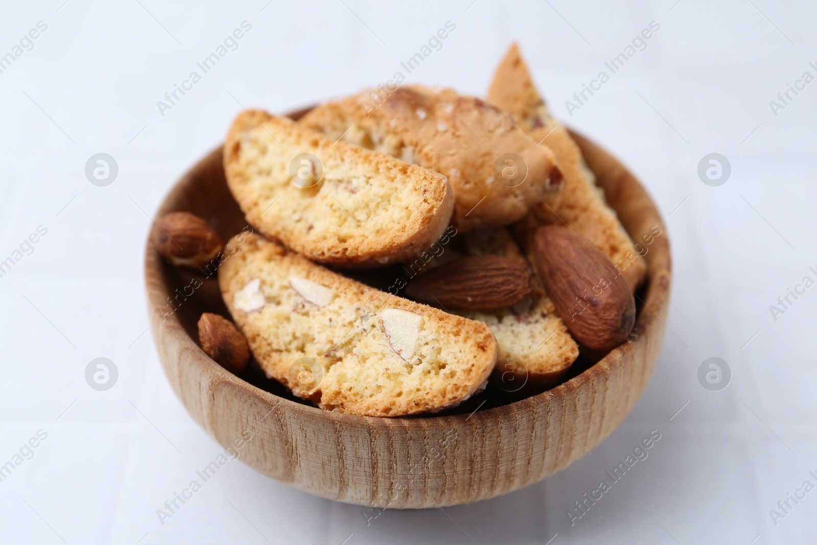 Photo of Tasty almond biscuits (Cantuccini) and nuts in bowl on white tiled table, closeup