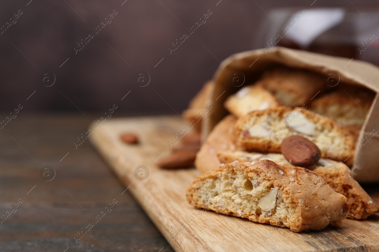 Photo of Paper bag with tasty almond biscuits (Cantuccini) and nuts on wooden table, closeup. Space for text