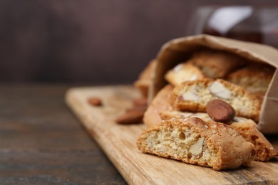 Photo of Paper bag with tasty almond biscuits (Cantuccini) and nuts on wooden table, closeup. Space for text