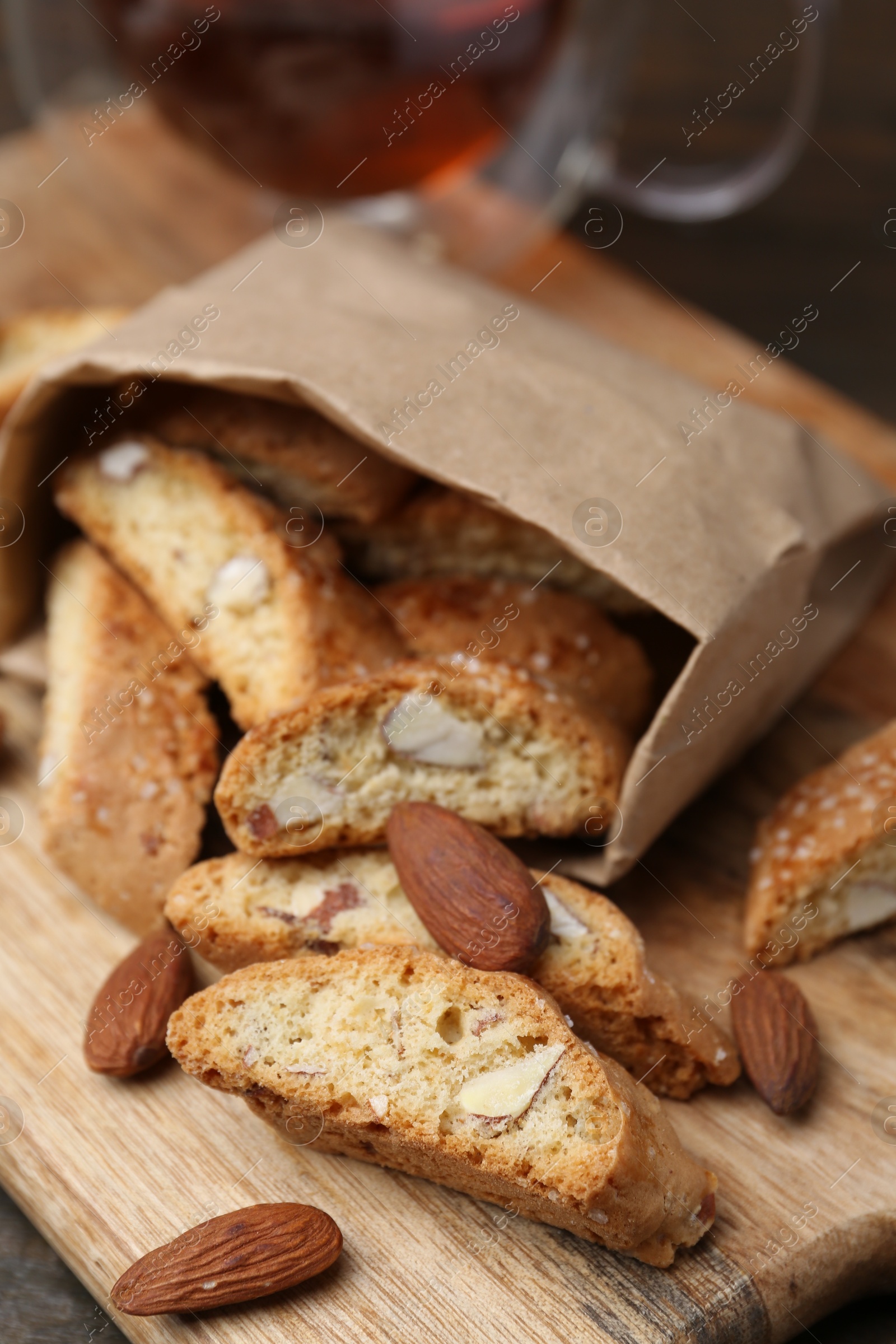 Photo of Paper bag with tasty almond biscuits (Cantuccini) and nuts on wooden board, closeup