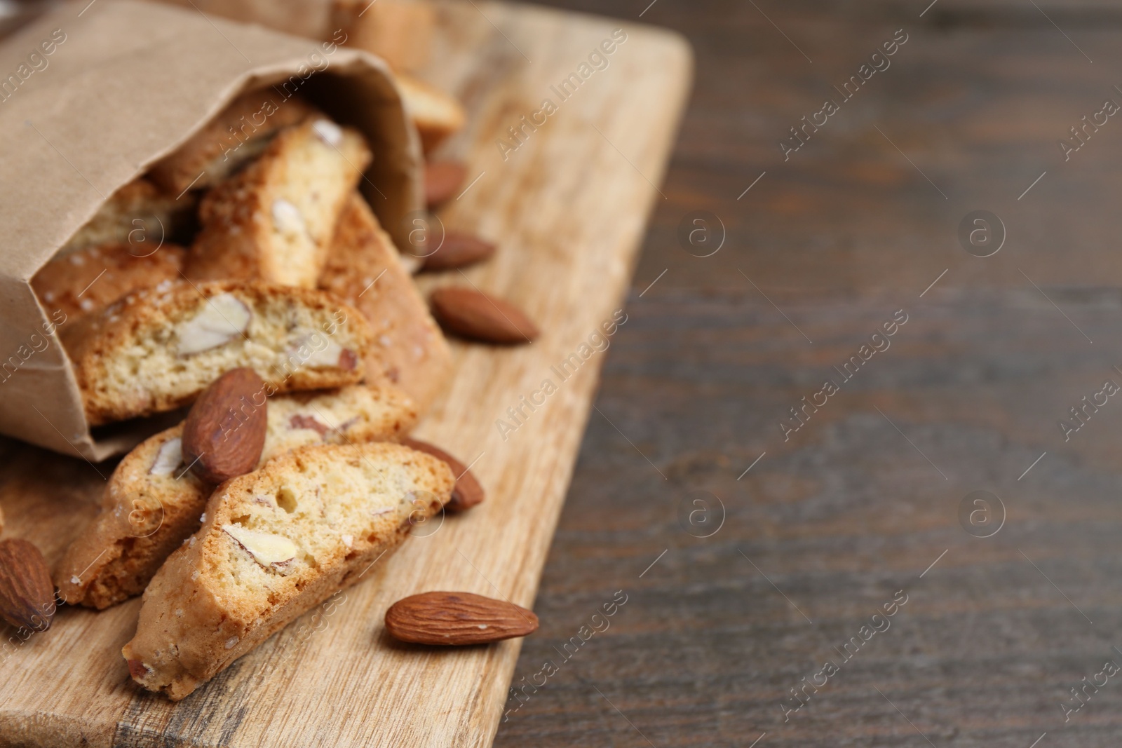 Photo of Paper bag with tasty almond biscuits (Cantuccini) and nuts on wooden table, closeup. Space for text