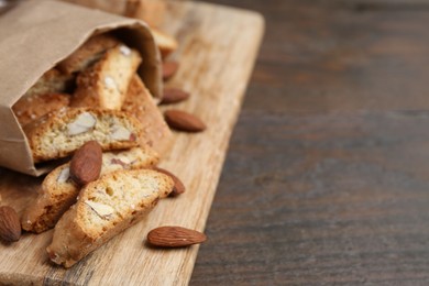 Photo of Paper bag with tasty almond biscuits (Cantuccini) and nuts on wooden table, closeup. Space for text