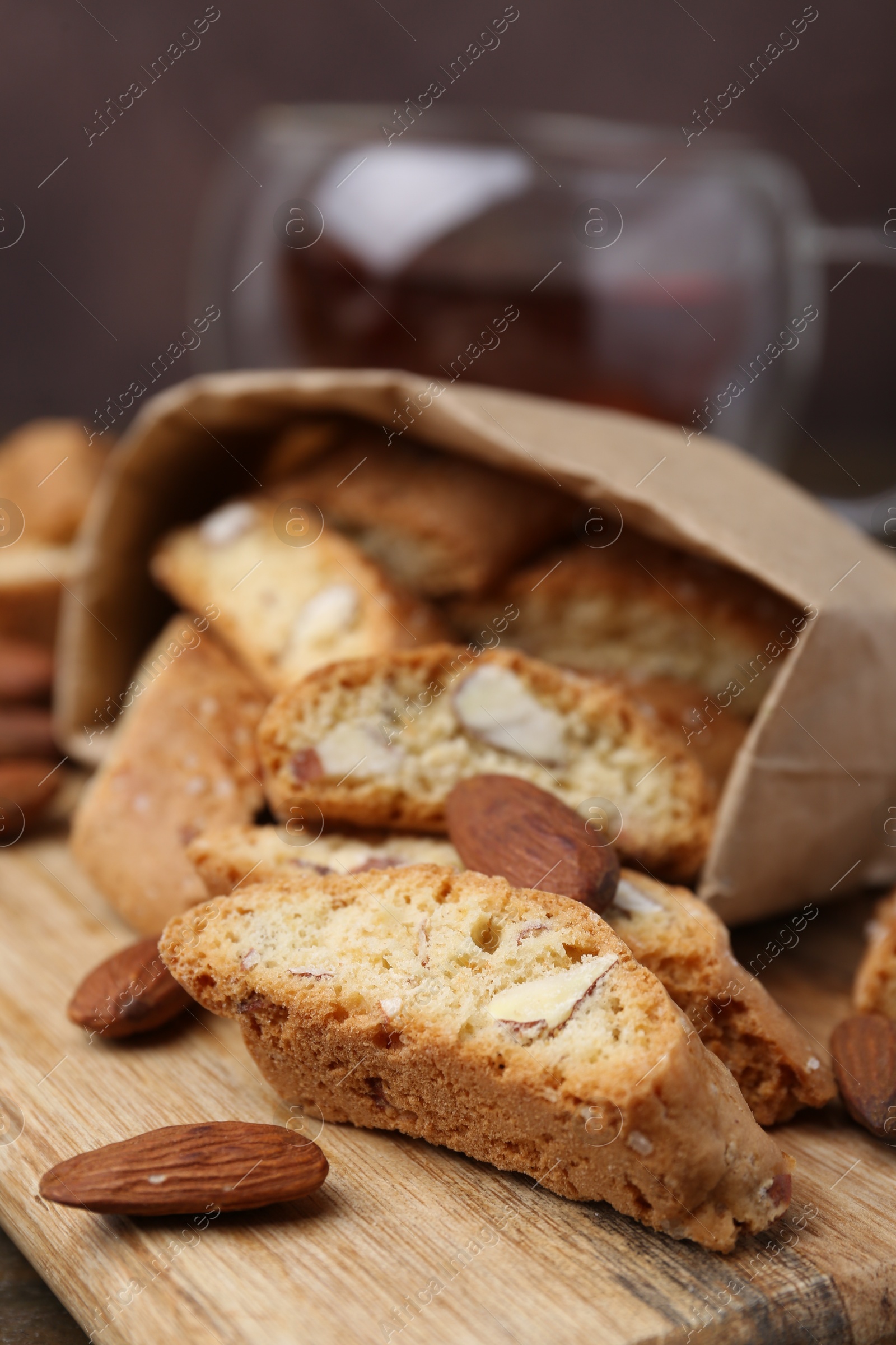 Photo of Paper bag with tasty almond biscuits (Cantuccini) and nuts on wooden board, closeup