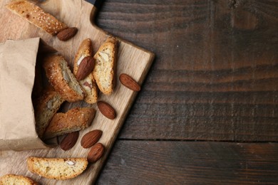 Photo of Paper bag with tasty almond biscuits (Cantuccini) and nuts on wooden table, top view. Space for text