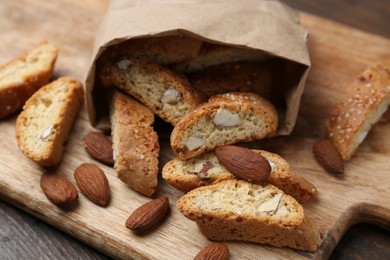 Photo of Paper bag with tasty almond biscuits (Cantuccini) and nuts on wooden table, closeup