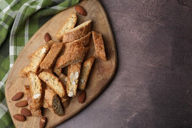 Photo of Tasty almond biscuits (Cantuccini) and nuts on brown textured table, top view. Space for text