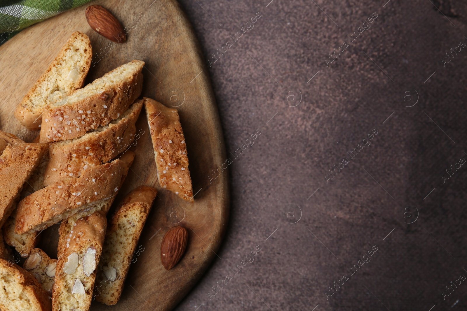 Photo of Tasty almond biscuits (Cantuccini) and nuts on brown textured table, top view. Space for text