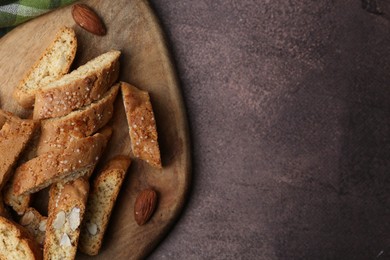 Photo of Tasty almond biscuits (Cantuccini) and nuts on brown textured table, top view. Space for text