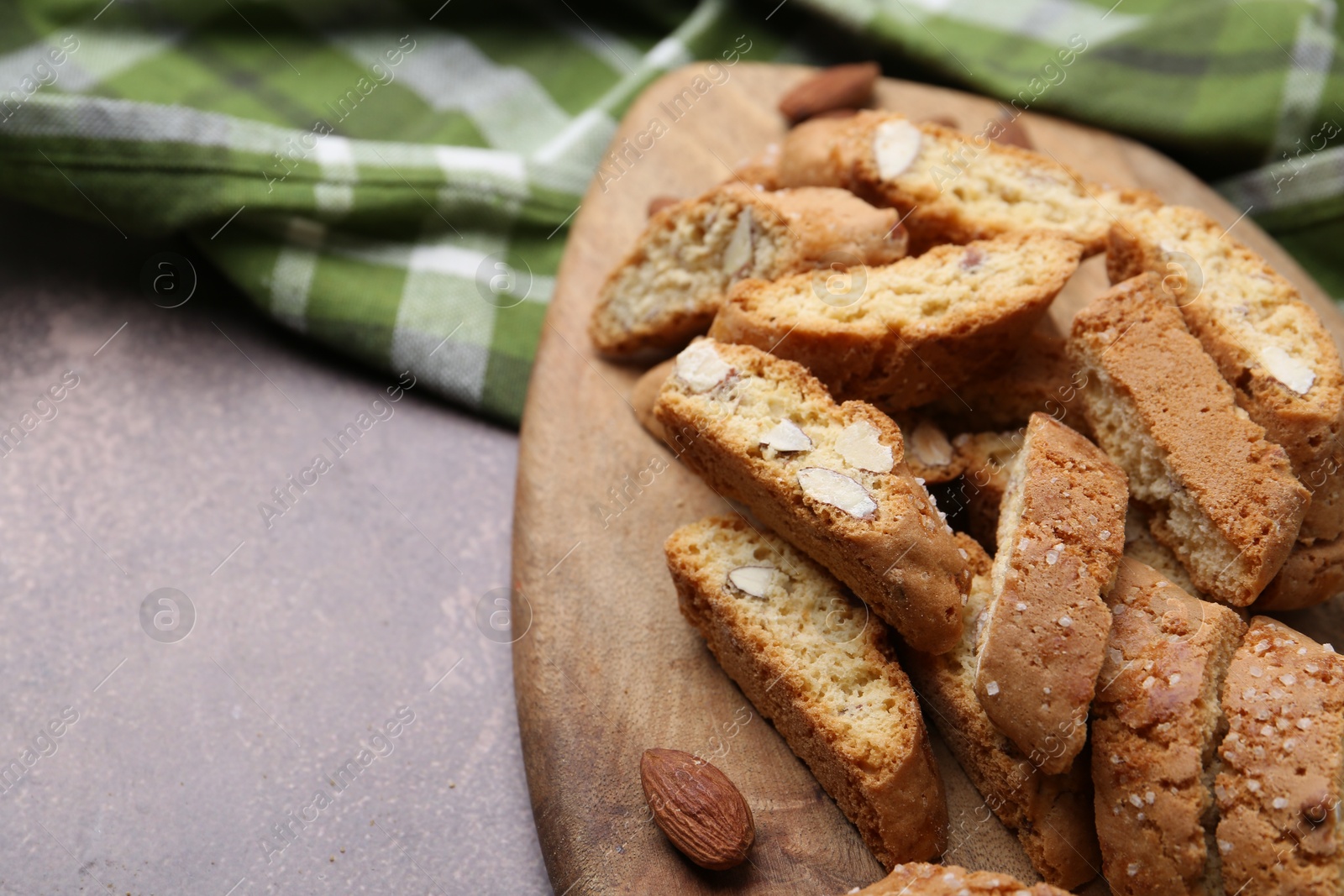 Photo of Tasty almond biscuits (Cantuccini) and nuts on brown textured table, closeup. Space for text