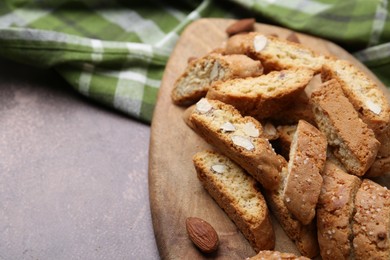 Photo of Tasty almond biscuits (Cantuccini) and nuts on brown textured table, closeup. Space for text