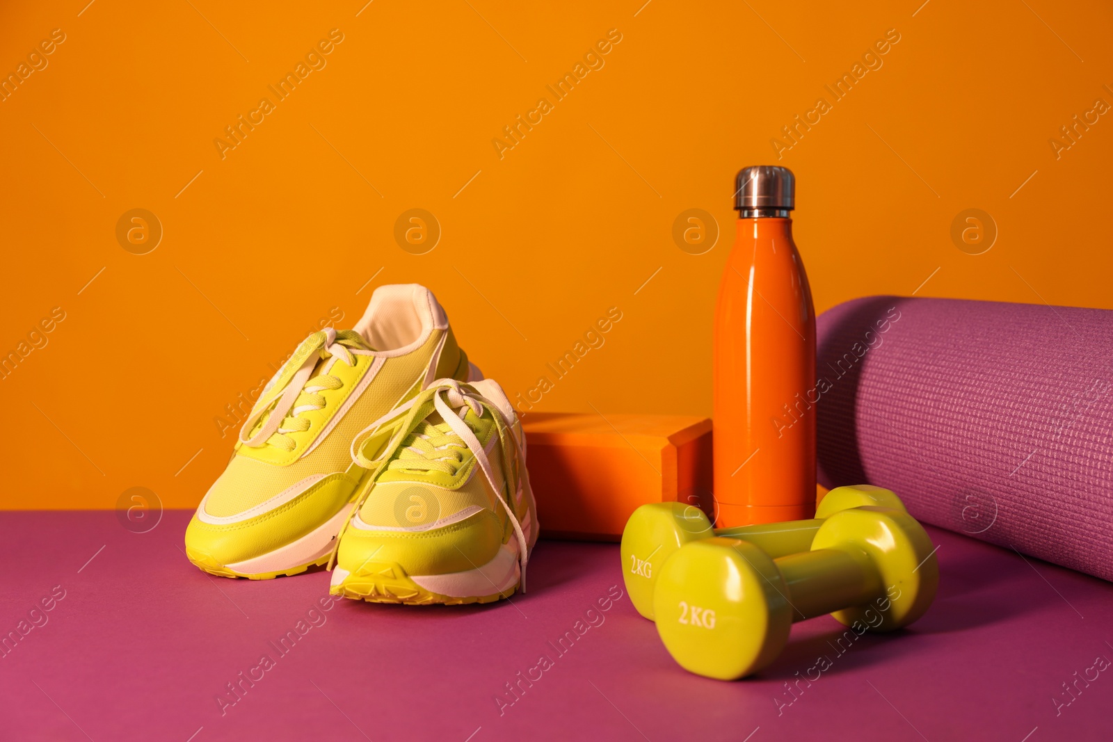 Photo of Stylish sneakers, thermo bottle and different sports equipment on color background