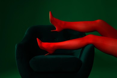 Photo of Woman in red tights and heels showing legs on green background, closeup