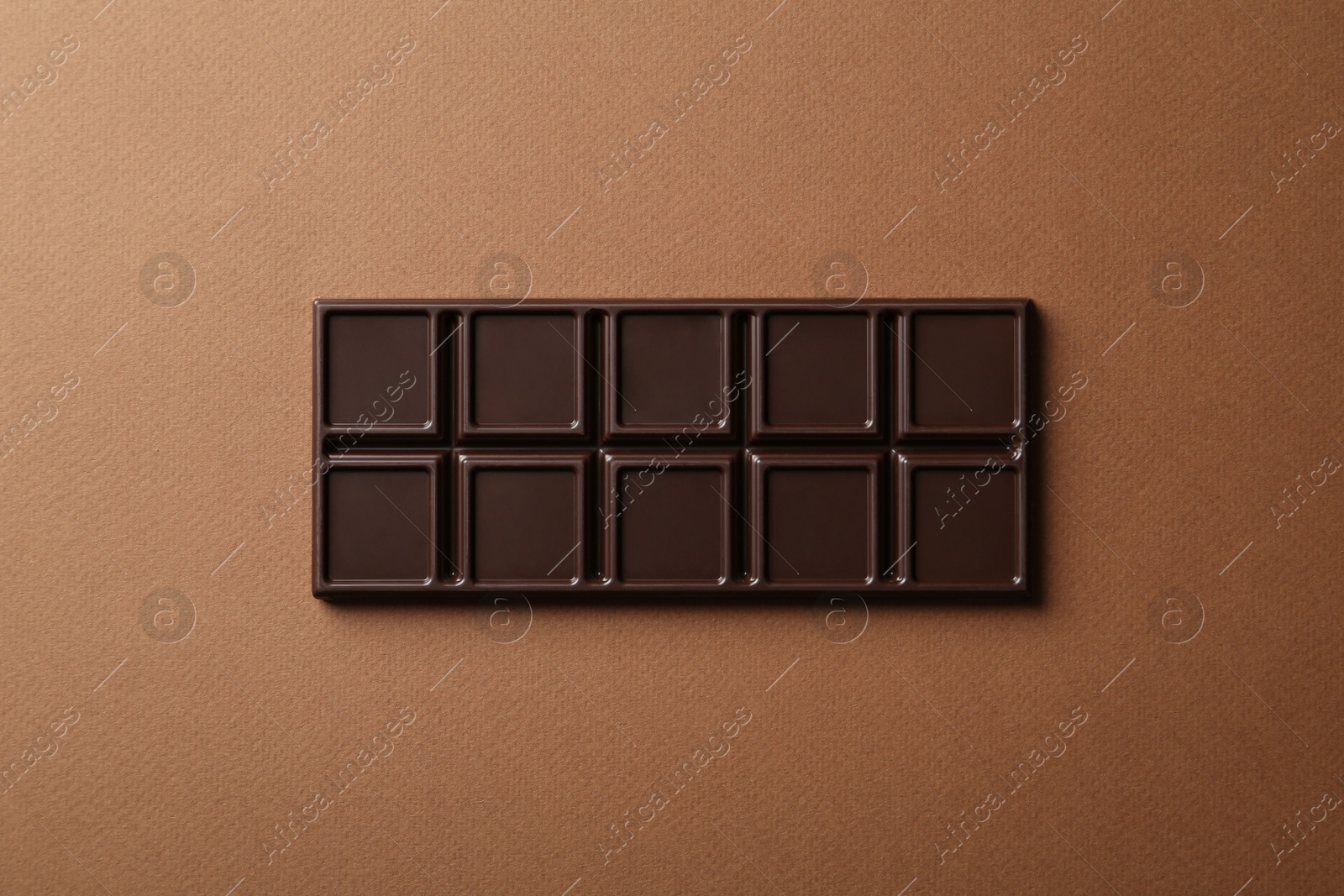 Photo of Tasty chocolate bar on brown background, top view