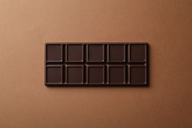 Photo of Tasty chocolate bar on brown background, top view