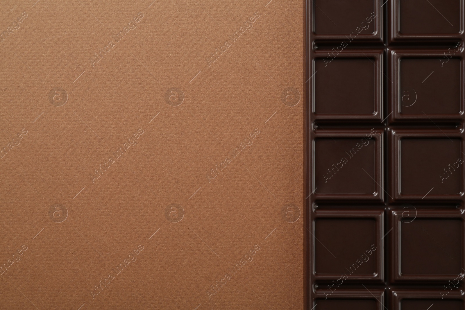 Photo of Tasty chocolate bar on brown background, top view. Space for text