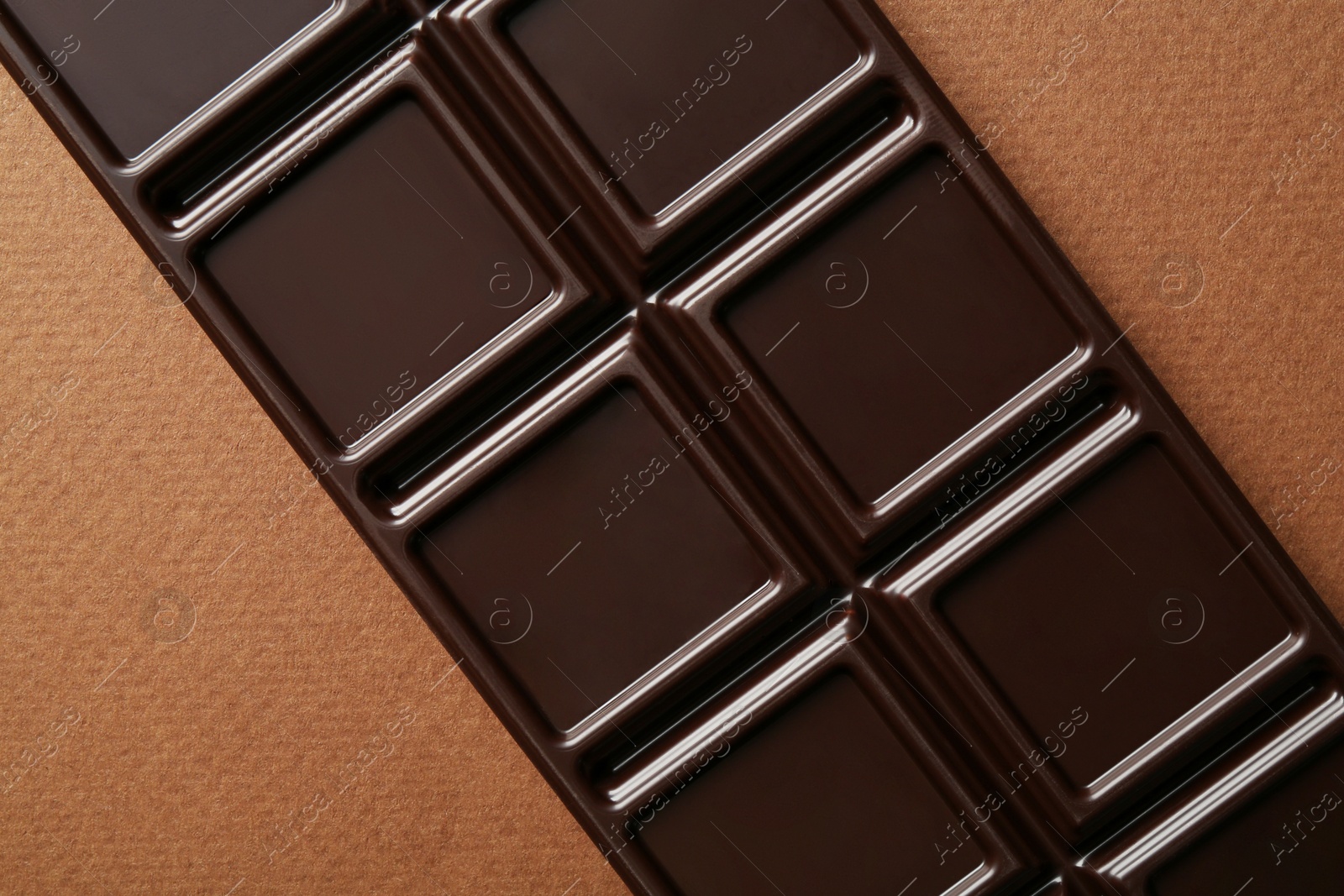 Photo of Tasty chocolate bar on brown background, top view