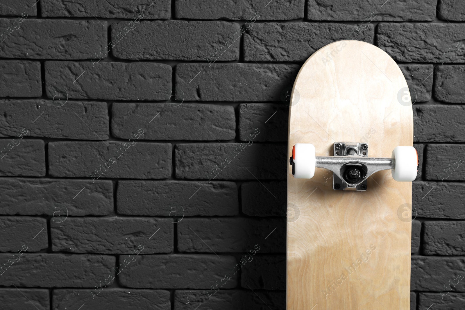 Photo of Modern skateboard near black brick wall. Space for text