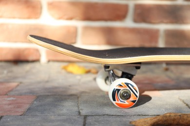 Photo of One skateboard on paved pathway near brick wall outdoors, closeup